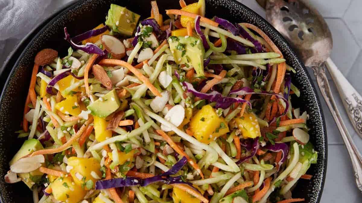 A bowl of broccoli salad next to mangoes.