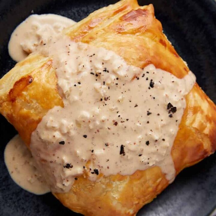 chicken in puff pastry with mustard cream sauce on top on a black plate on a gray towel.