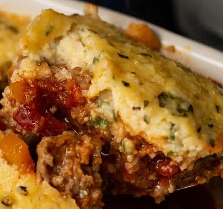 A casserole dish of chili topped with cheesy grits.