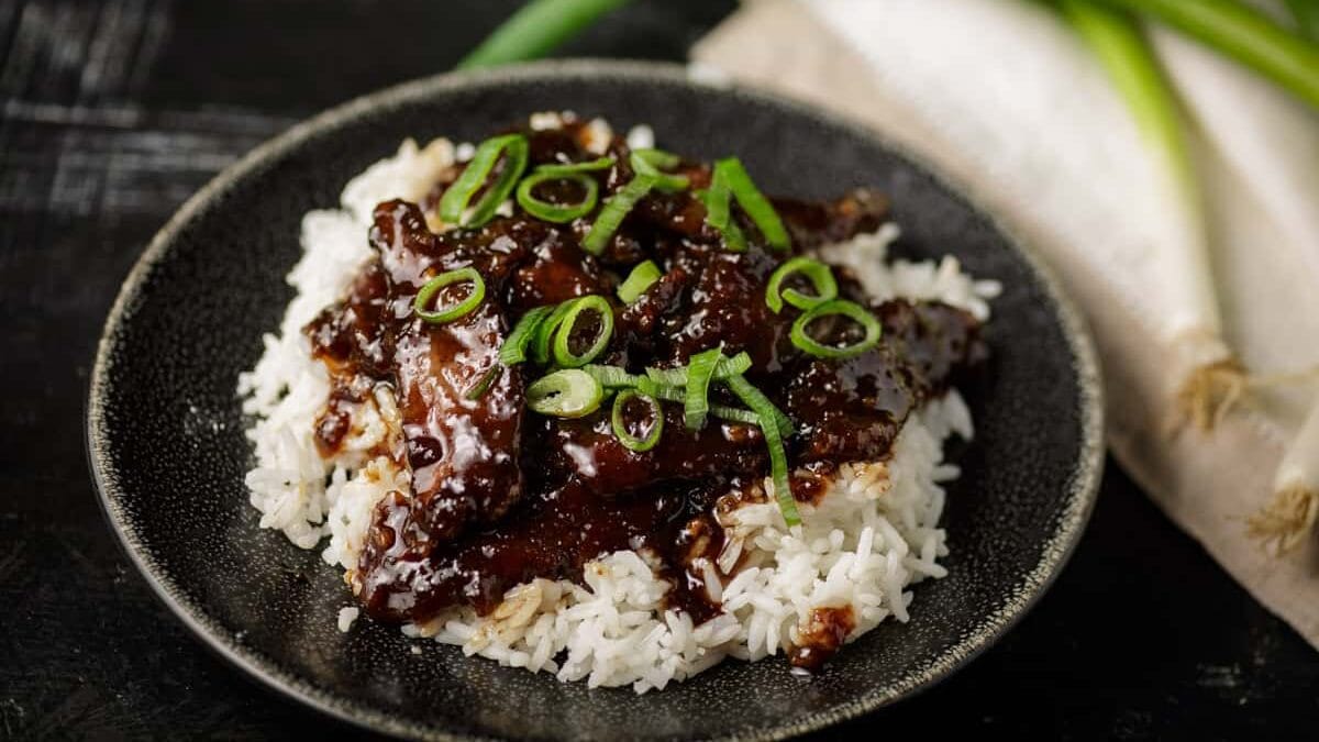 Mongolian beef stir fry over rice on a black platter.