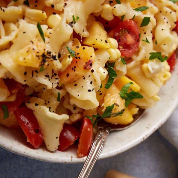 A bowl of peach pasta salad with the dressing in a pitcher.