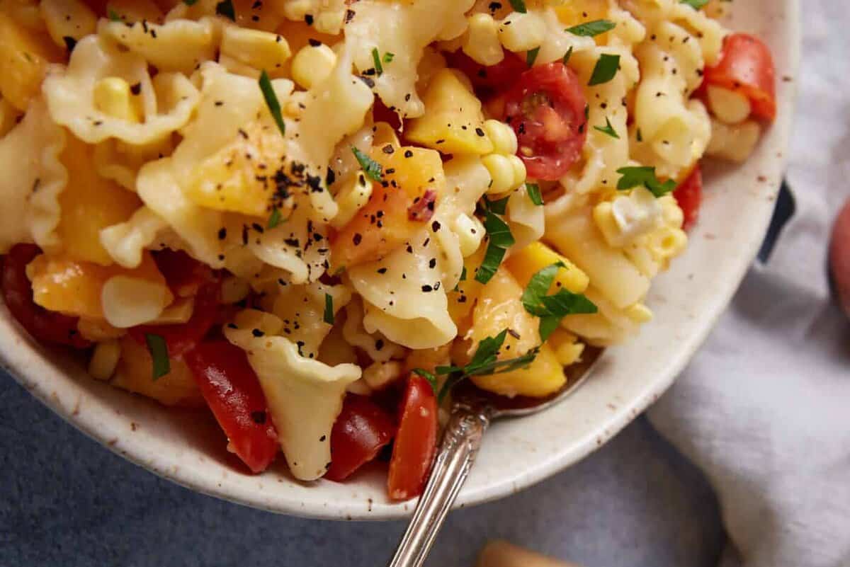 A bowl of peach pasta salad with the dressing in a pitcher.