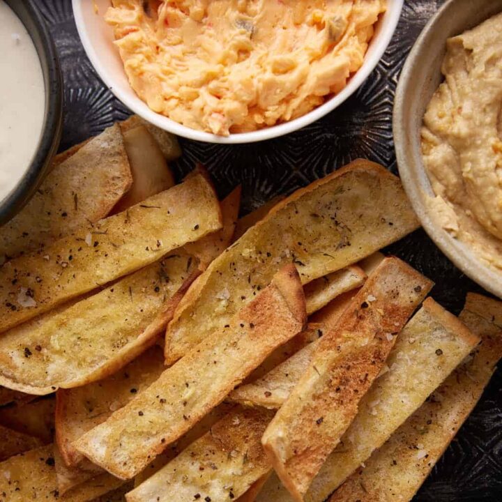 Baked pita chips next to bowls of dip.