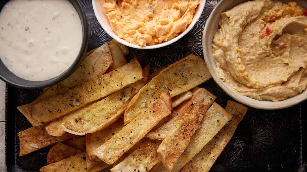 Baked pita chips next to bowls of dip.