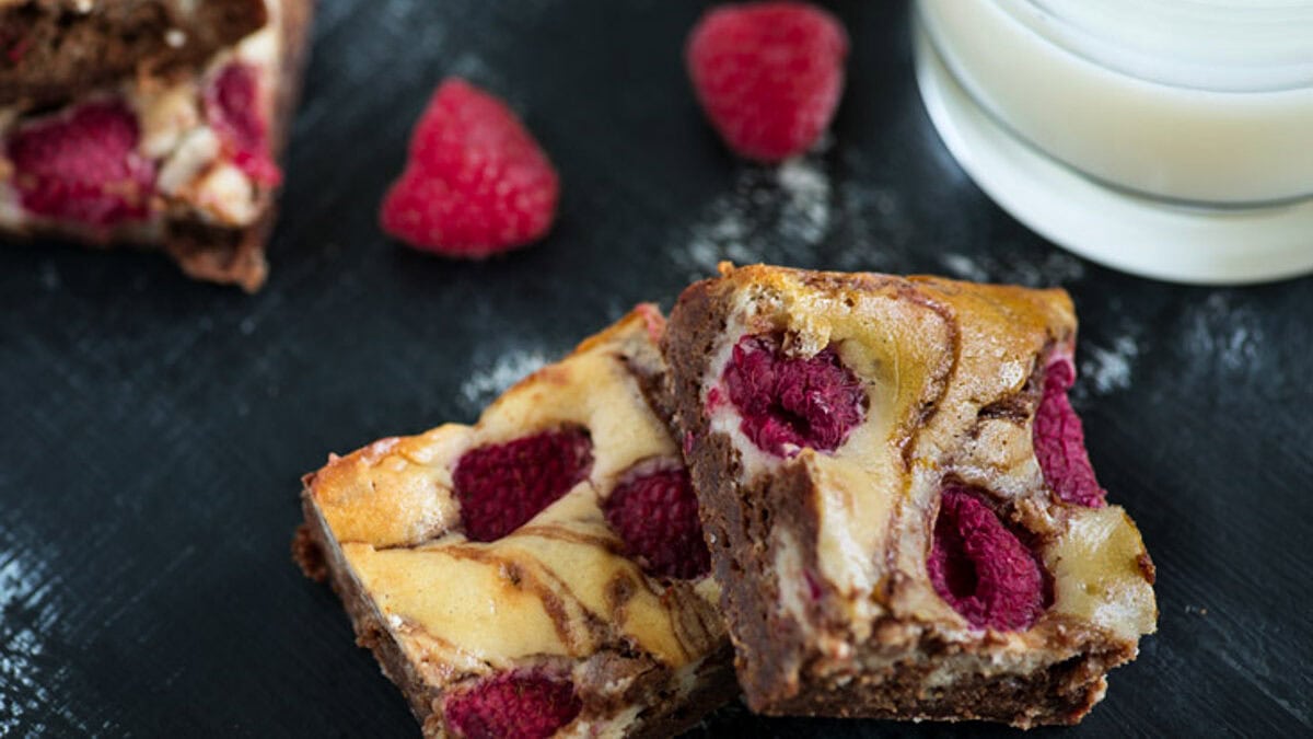Fudgy brownies with fresh raspberries on a black counter