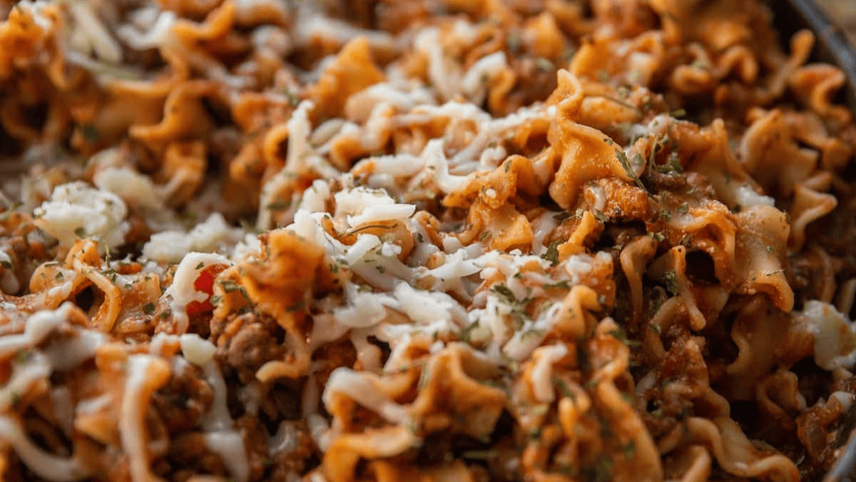 Close-up of lasagna noodles mixed with ground meat, tomato sauce, and melted cheese, garnished with herbs. The dish appears hearty and rich, with a golden, cheesy texture.