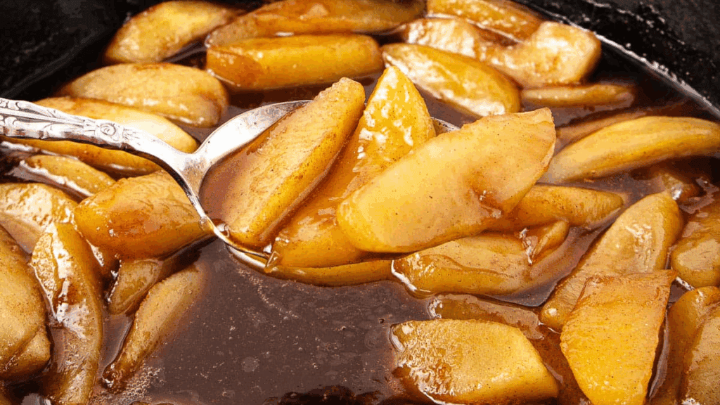 Sliced apples cooked in a glossy cinnamon sauce, with a spoon lifting some of the apples from the mixture.