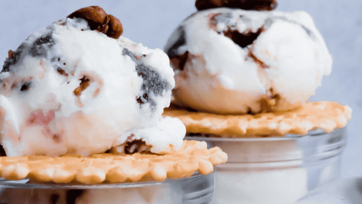 Two scoops of vanilla ice cream with chocolate swirls and nuts sit on top of round crackers, placed on small glass containers, against a light background.
