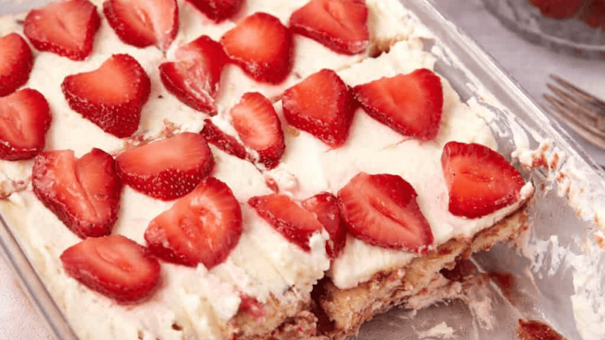A glass dish filled with creamy dessert topped with sliced strawberries; some pieces have been cut and removed, revealing layers inside.