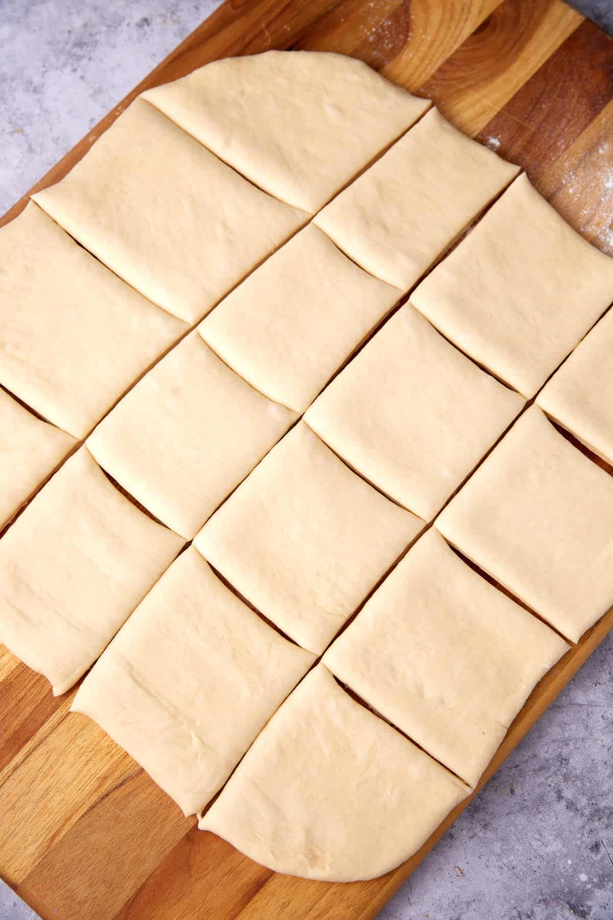 A sheet of dough cut into even rectangular pieces sits on a wooden cutting board, ready to be used for baking. The surface beneath the board appears to be a gray countertop.