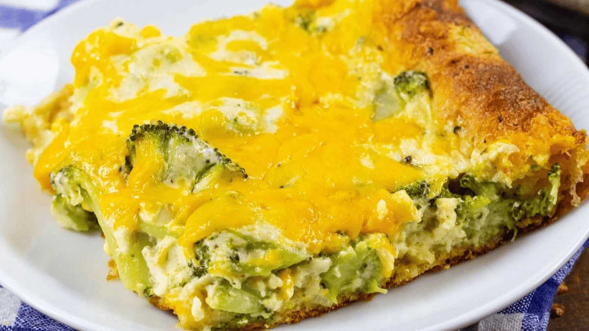 A slice of cheesy broccoli casserole with a golden, melted cheese topping, served on a white plate.