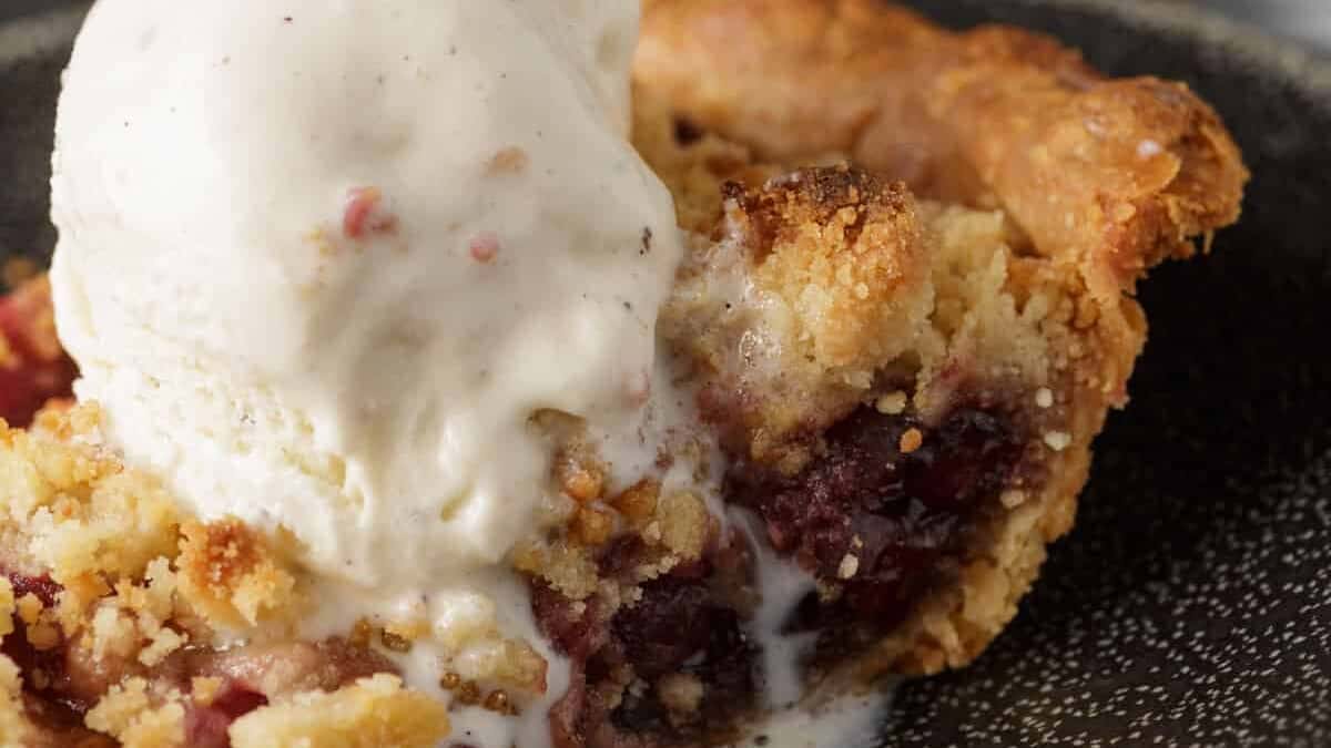 A slice of cherry pie with a scoop of ice cream.