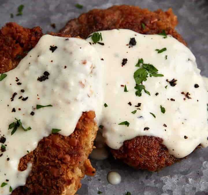 A plate with two pieces of chicken fried steak with milk gravy.