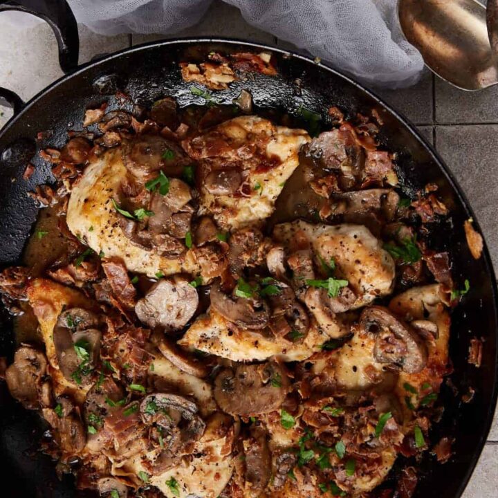 A skillet of chicken marsala next to serving spoons.