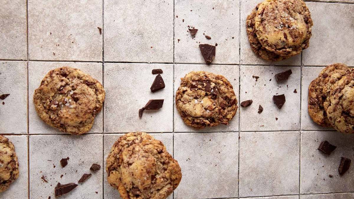 Chocolate chip cookies and chunks of chocolate scattered on a tiled surface.