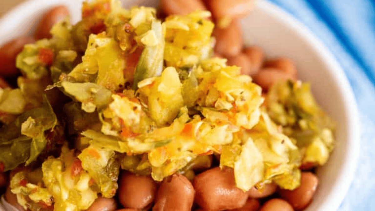 A close-up of a bowl filled with pink beans topped with a generous serving of colorful, chopped vegetable relish.