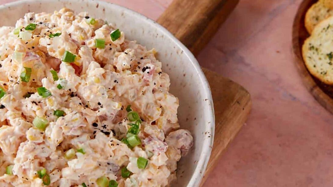 Corn dip in a bowl on a wooden platter.