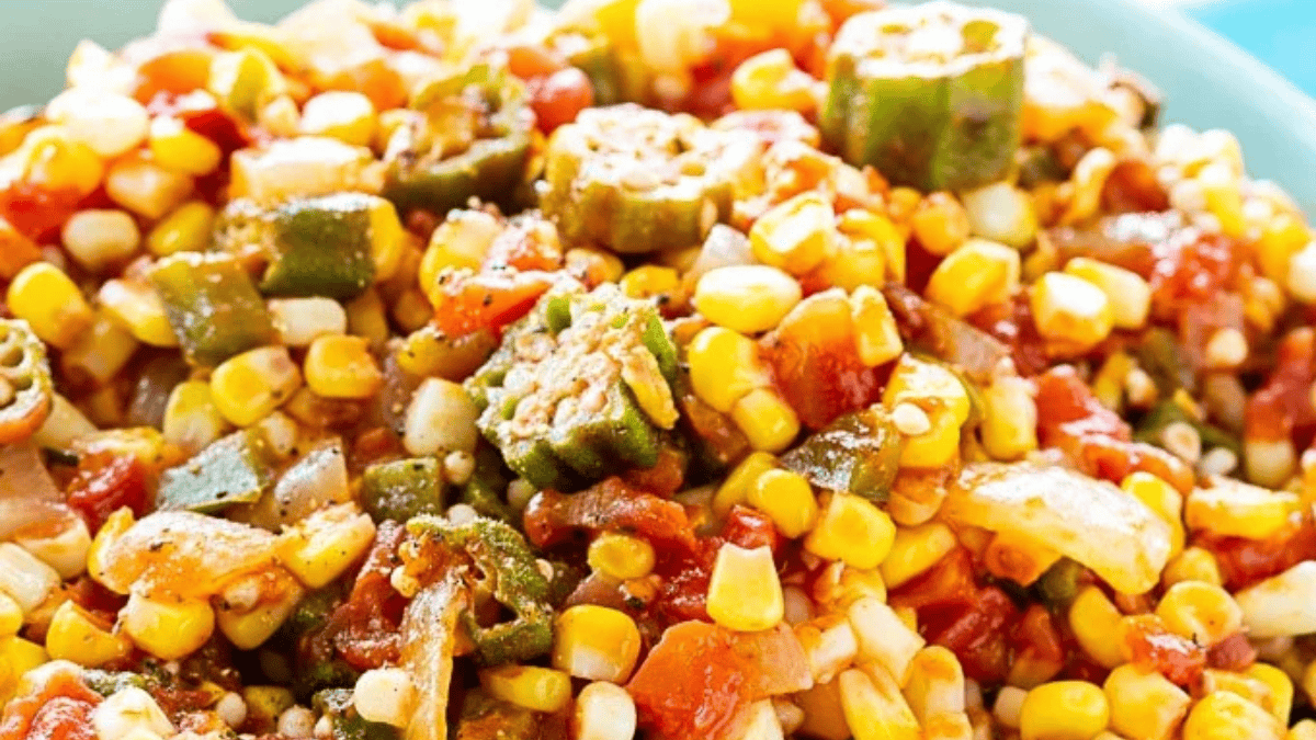 A close-up of a colorful vegetable medley featuring corn, diced tomatoes, onions, and sliced okra, all mixed together and seasoned, served in a light blue bowl.