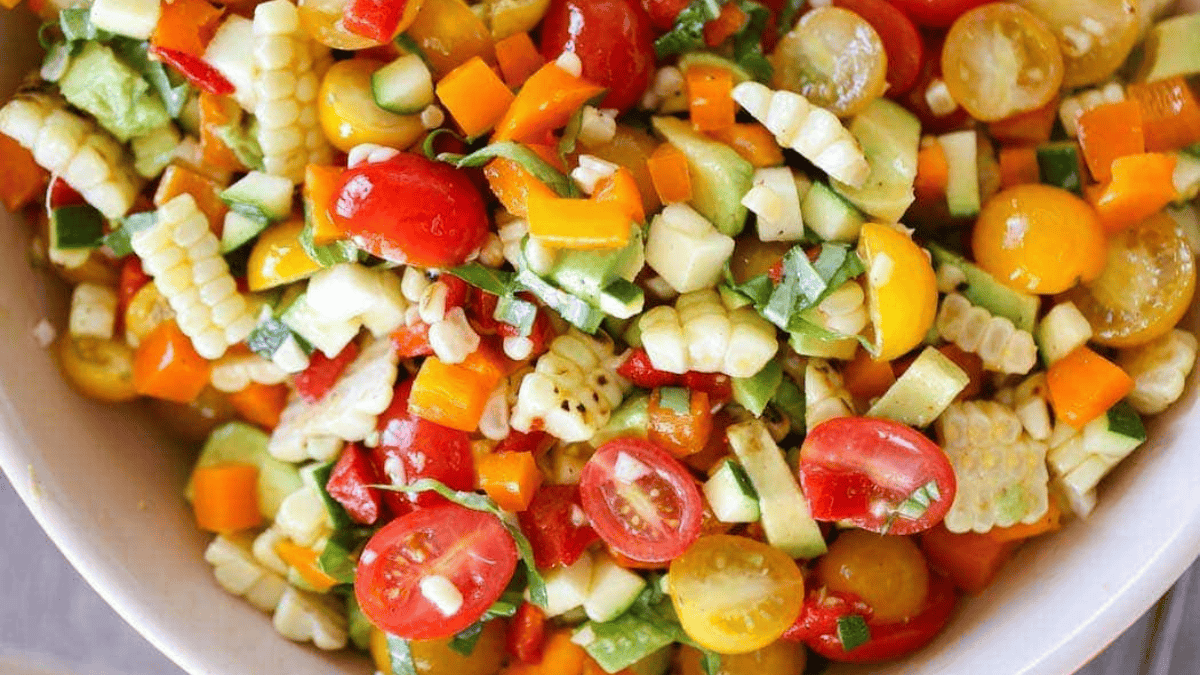 A colorful salad featuring chopped cherry tomatoes, corn, bell peppers, zucchini, and fresh herbs, all mixed together in a bowl.