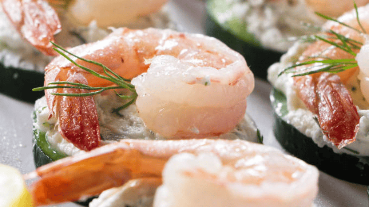 Close-up of shrimp appetizers served on cucumber slices with a creamy white topping and garnished with fresh dill.
