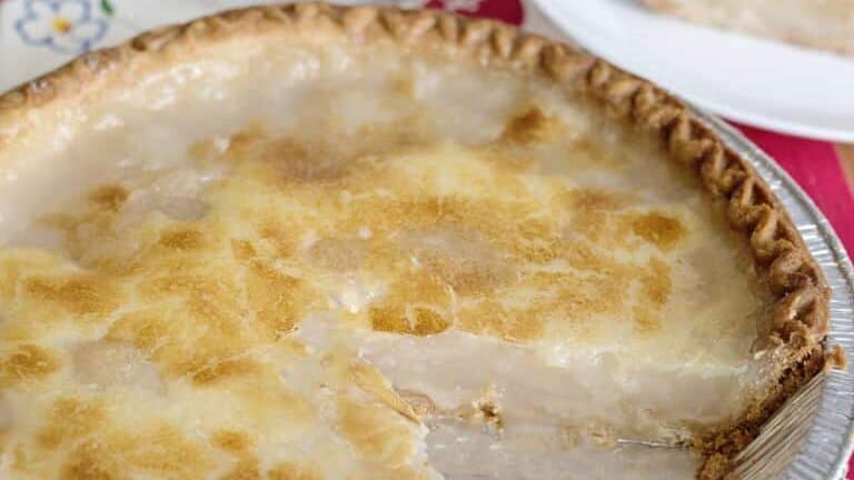 A creamy custard pie with a golden-brown top, once cherished but now among these once popular foods are fading fast. One slice sits on a white plate beside a glass of ice water; the rest is in a foil pan on a colorful, patterned cloth.