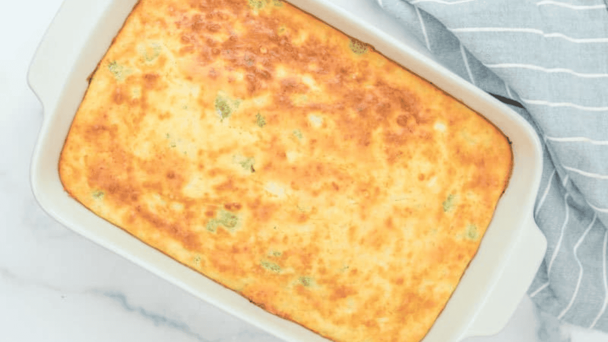 A baked casserole with a golden-brown top sits in a white baking dish next to a folded blue and white striped kitchen towel.