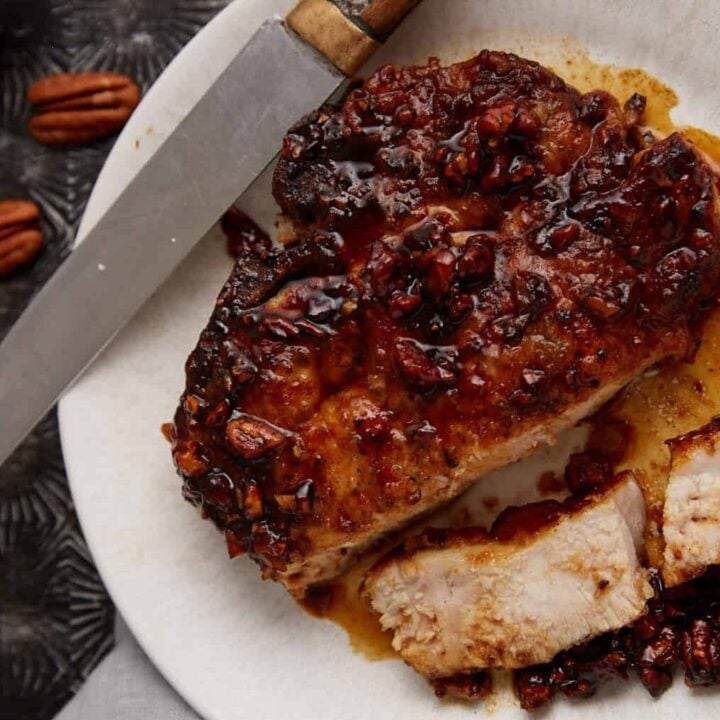 A pecan honey glazed pork chop on a plate with a fork.