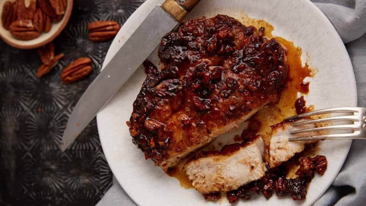 A pecan honey glazed pork chop on a plate with a fork.