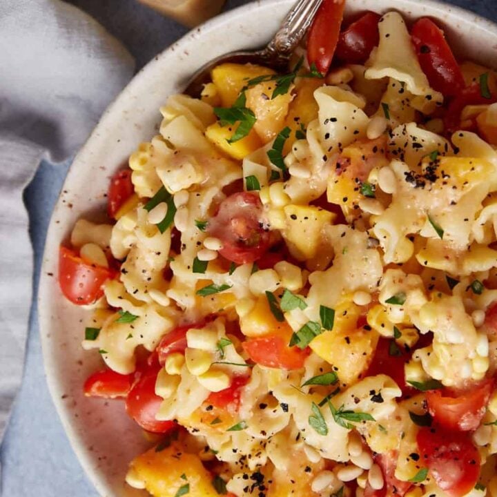 A pasta salad with peaches, corn and tomatoes in a serving bowl.