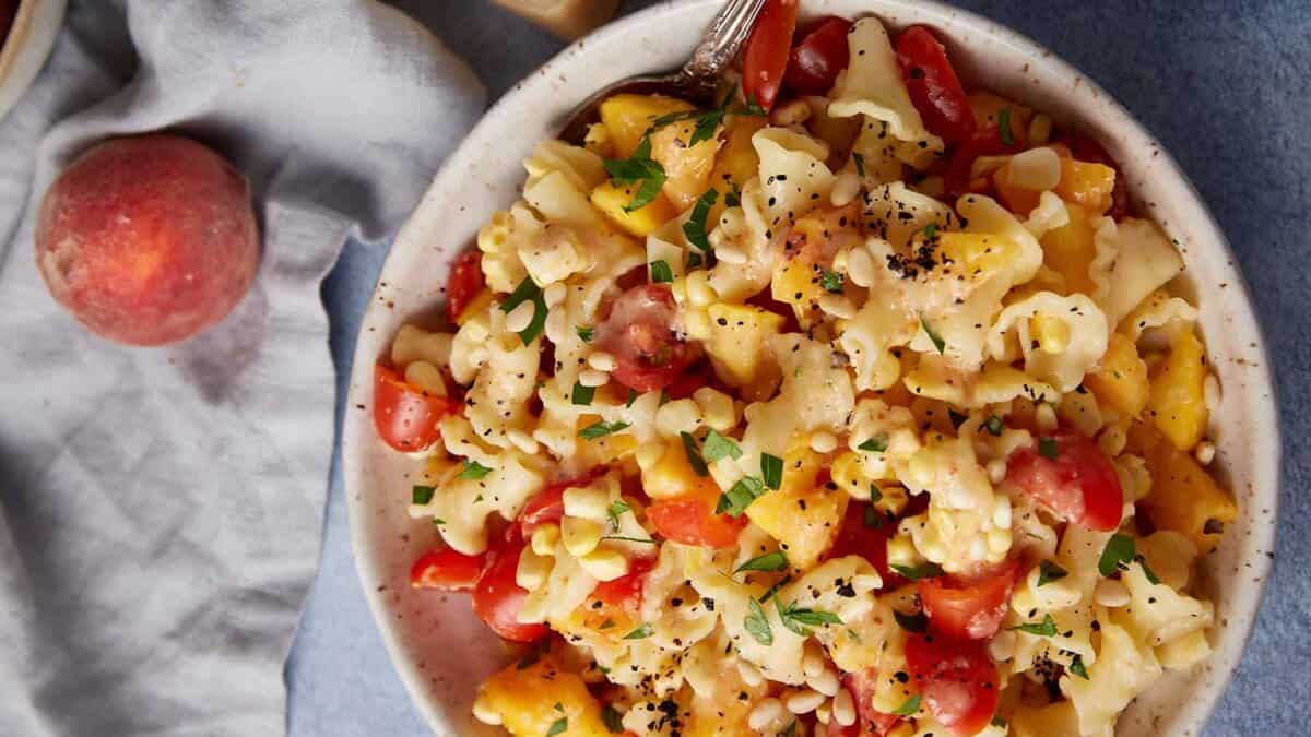 A pasta salad with peaches, corn and tomatoes in a serving bowl.