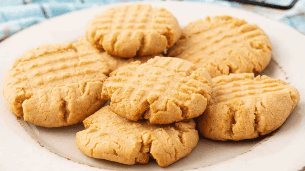 A plate of classic peanut butter cookies, each with a crisscross fork pattern on top, arranged in a casual pile on a white plate.