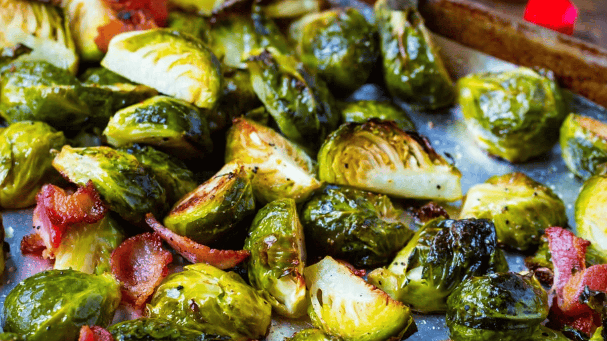 Roasted Brussels sprouts and crispy bacon pieces on a baking sheet, with caramelized edges and a golden-brown finish.
