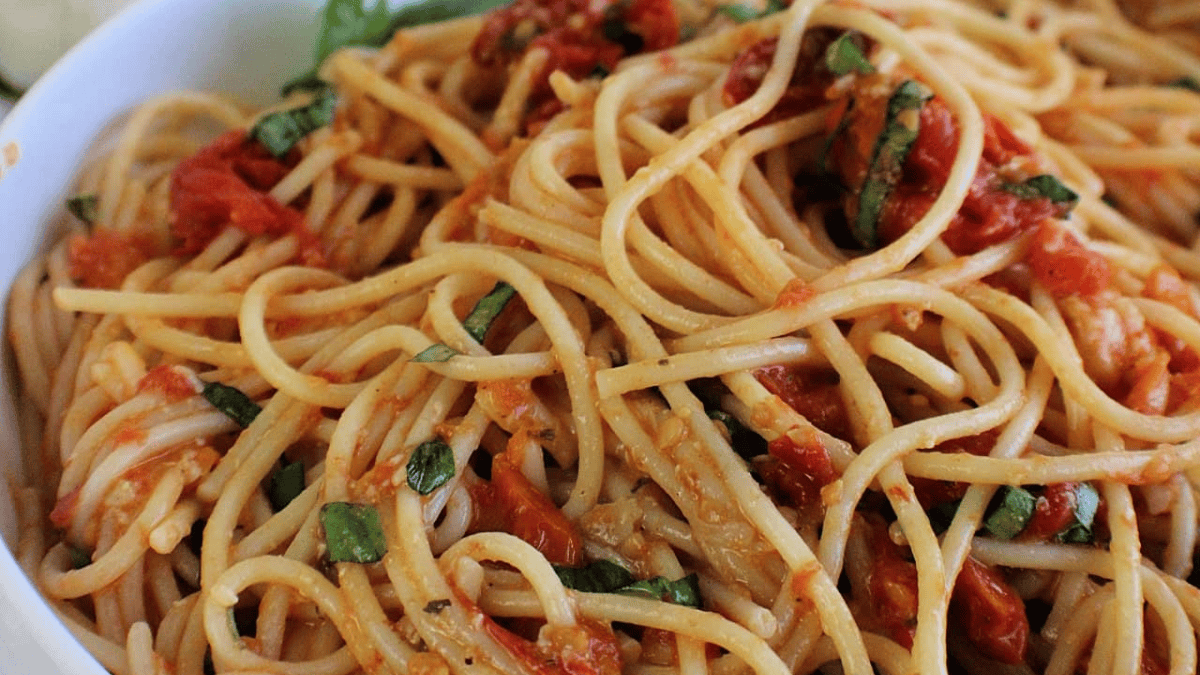 A close-up of a plate of spaghetti tossed with tomato sauce, fresh basil, and bits of tomato, showing a flavorful and colorful pasta dish.