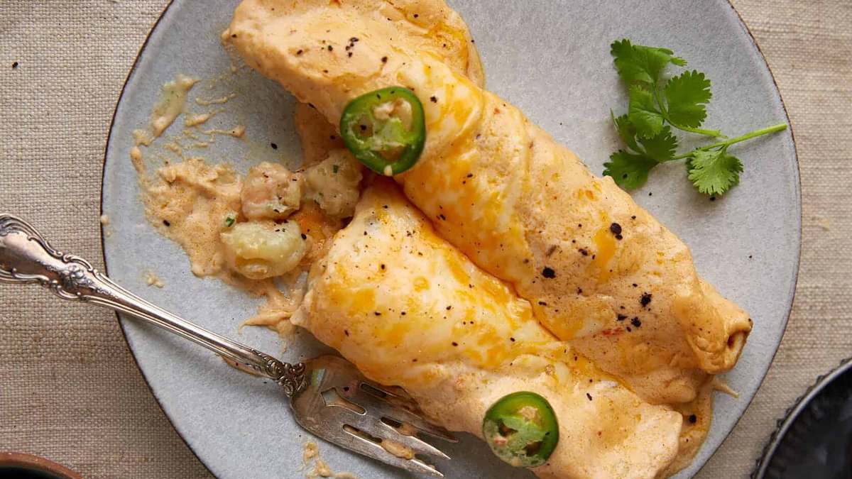 Two shrimp enchilada on a plate with a fork.