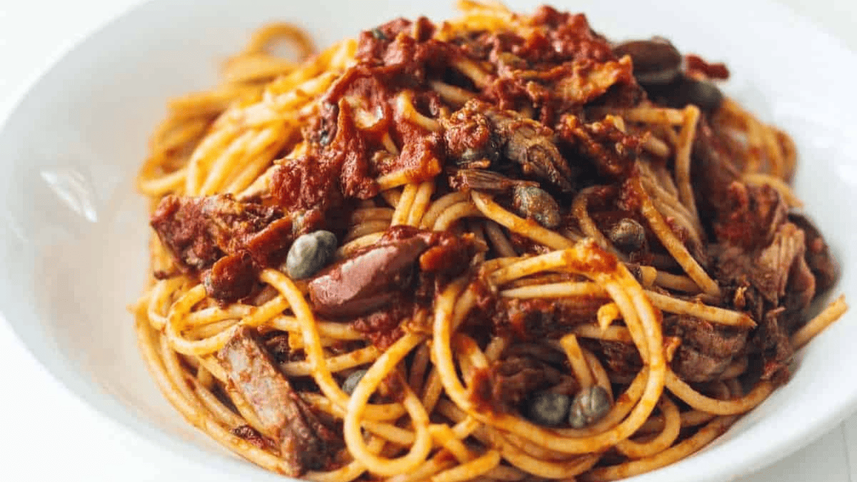 A plate of spaghetti topped with tomato sauce, pieces of meat, capers, and olives, served in a white bowl.