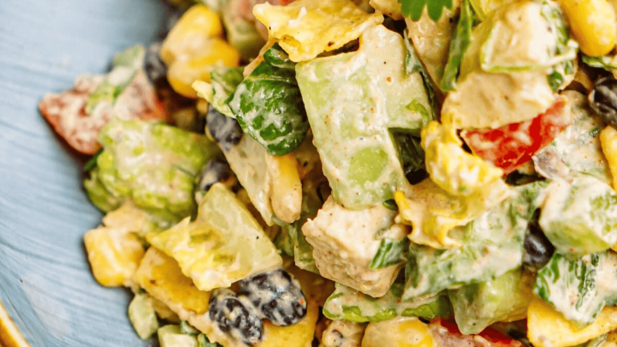 Close-up of a colorful salad with diced chicken, black beans, corn, lettuce, tomatoes, green bell peppers, and creamy dressing, served in a blue bowl.