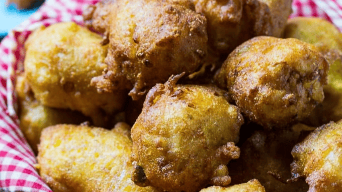 A close-up of a basket filled with golden-brown hush puppies resting on a red and white checkered cloth.
