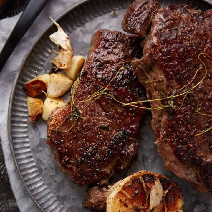 Ribeye steaks on a platter next to a roasted garlic.