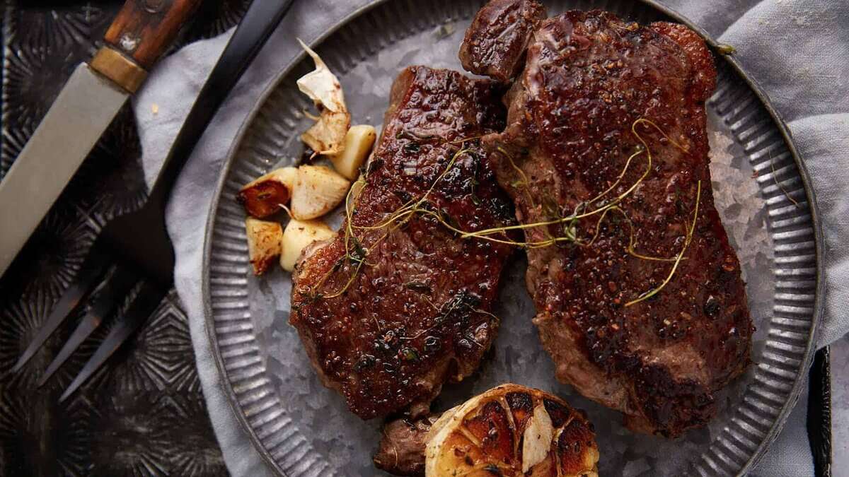 Ribeye steaks on a platter next to a roasted garlic.
