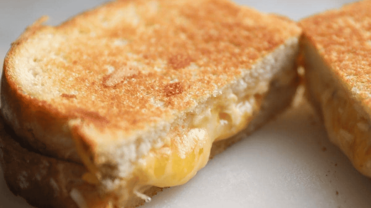 Close-up of a golden-brown grilled cheese sandwich, cut in half to reveal melted cheese oozing between two slices of toasted bread.