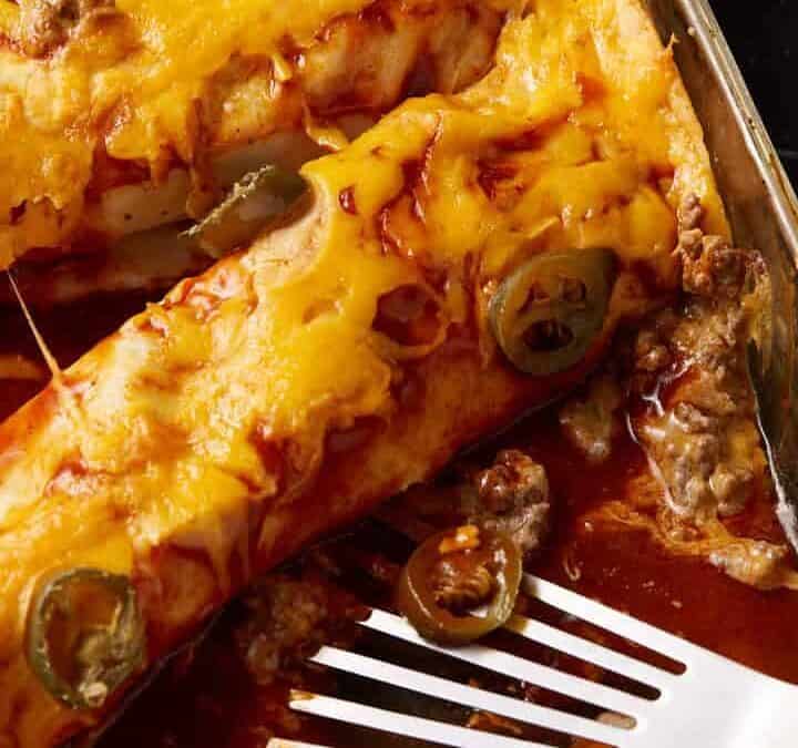 A baking dish with beef enchiladas and a spatula.