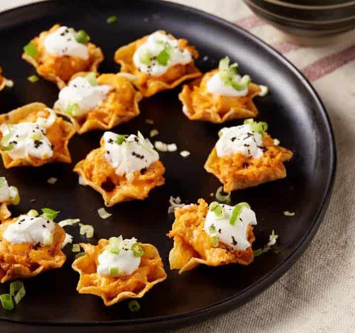 A platter of chicken bites next to a bowl of sour cream and green onions.