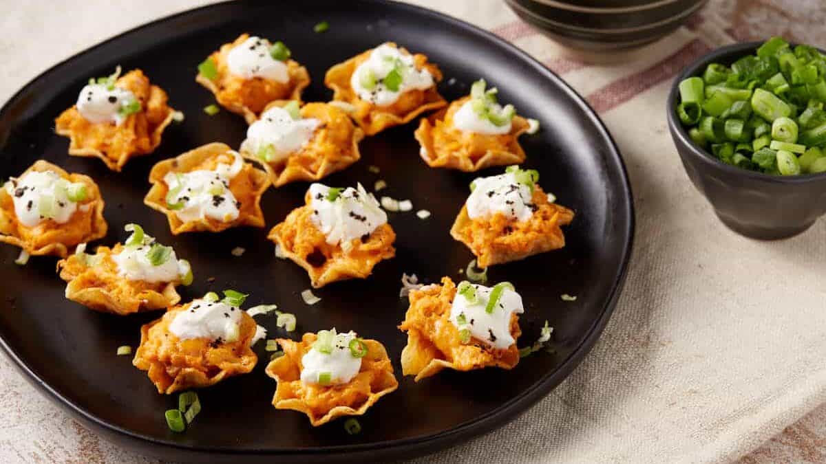 A platter of chicken bites next to a bowl of sour cream and green onions.