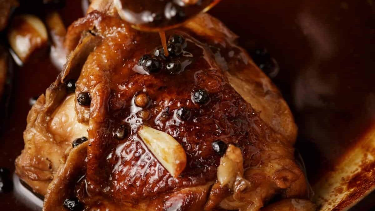 Sauce on a spoon with garlic over a chicken thigh