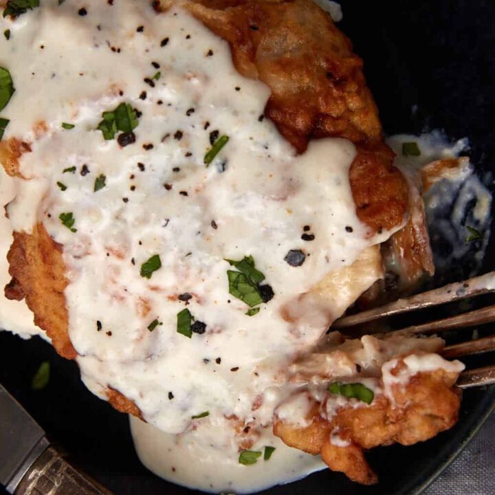 chicken fried chicken with gravy on a black plate being cut into with a fork.