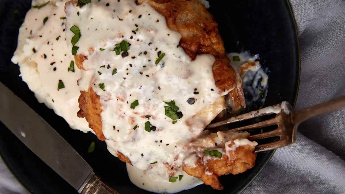 chicken fried chicken with gravy on a black plate being cut into with a fork.