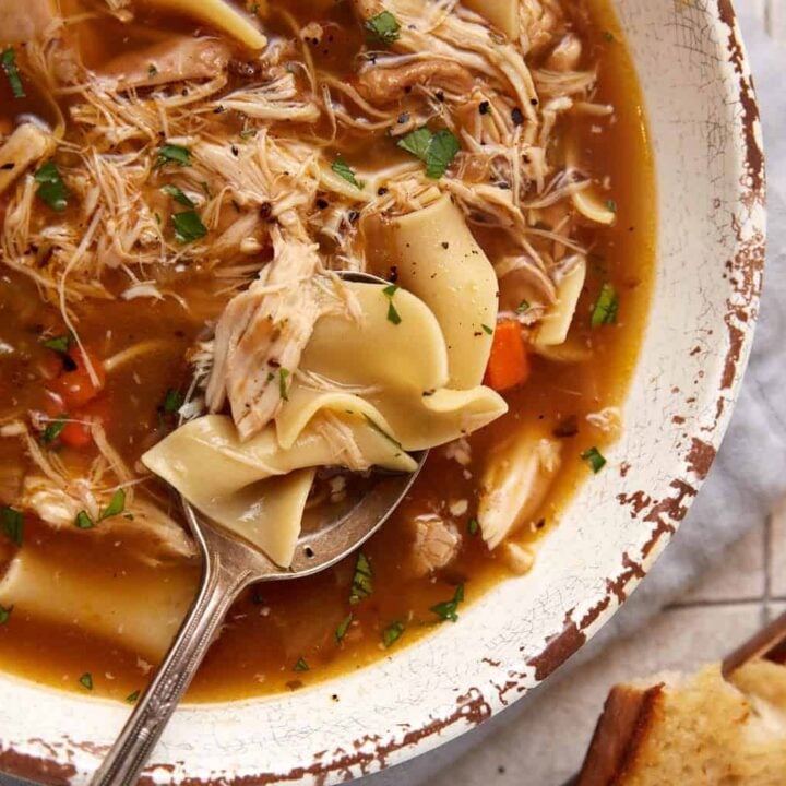 A spoon in a bowl of slow cooker chicken noodle soup.