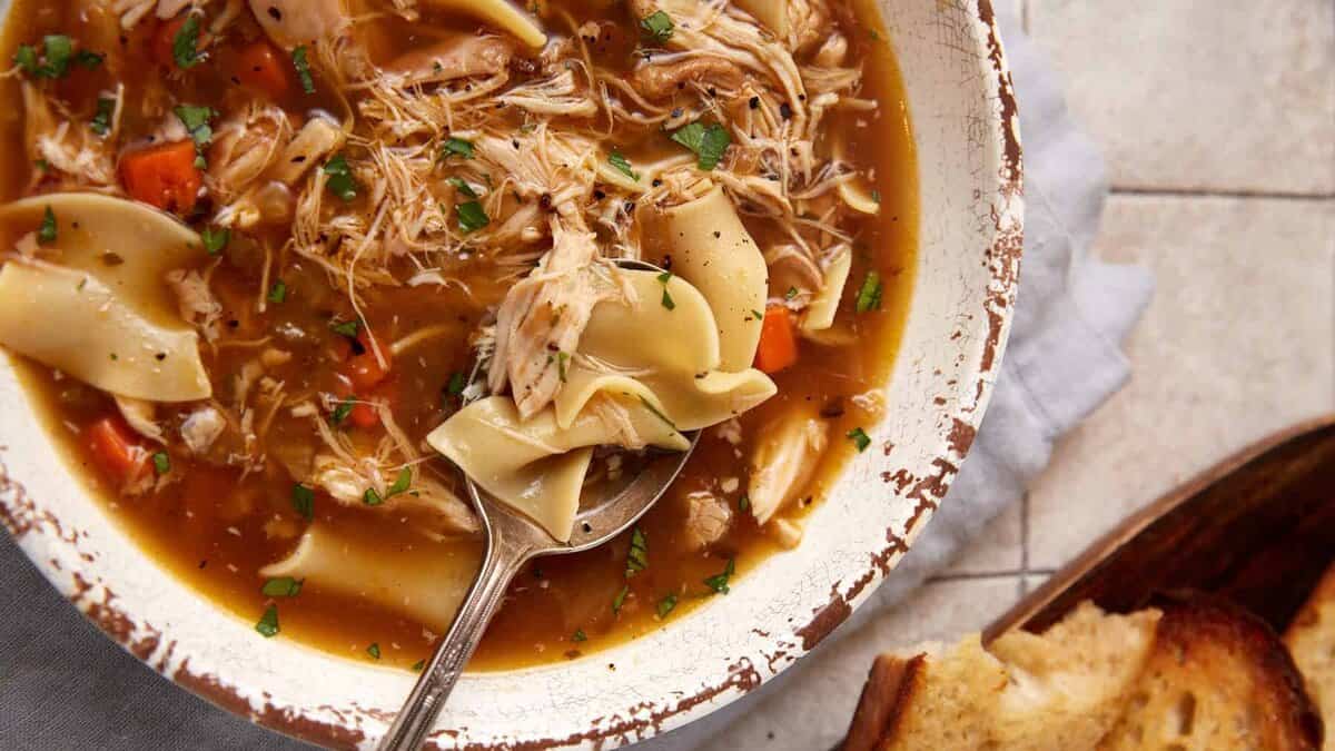 A spoon in a bowl of slow cooker chicken noodle soup.