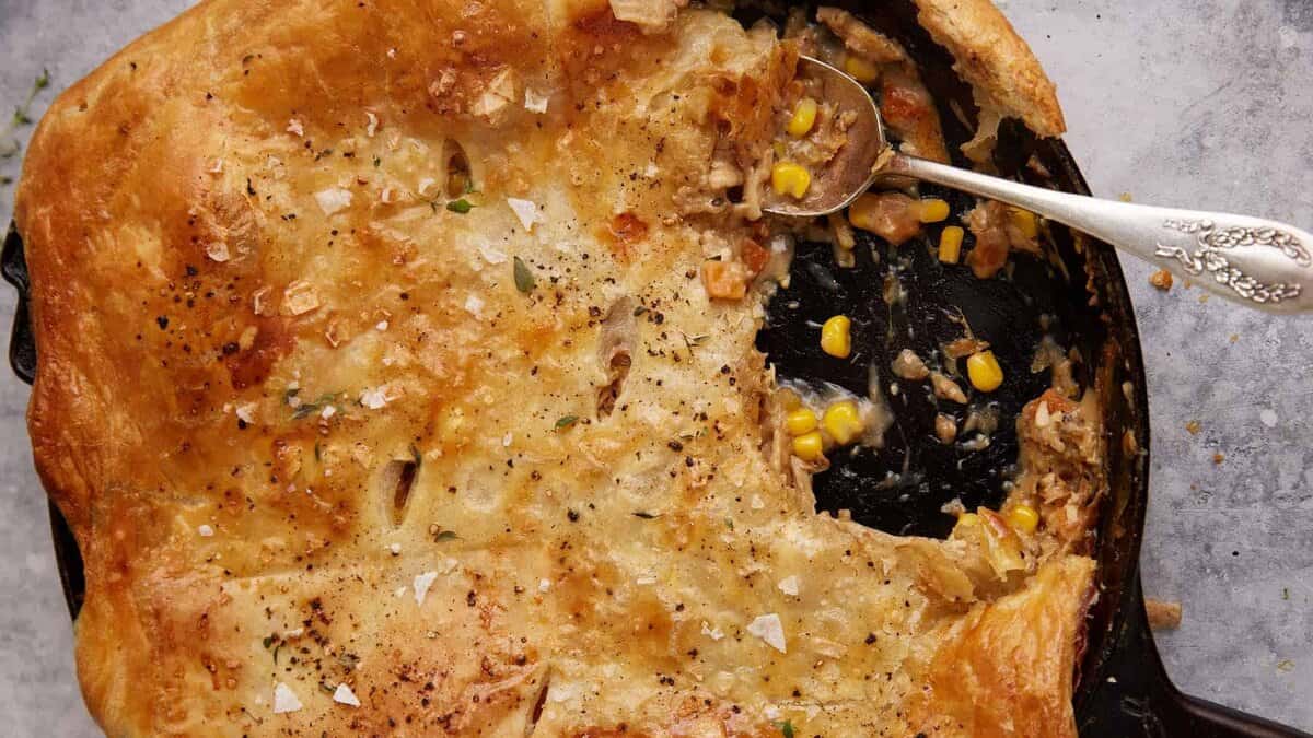 A skillet of chicken pot pie covered with puff pastry.