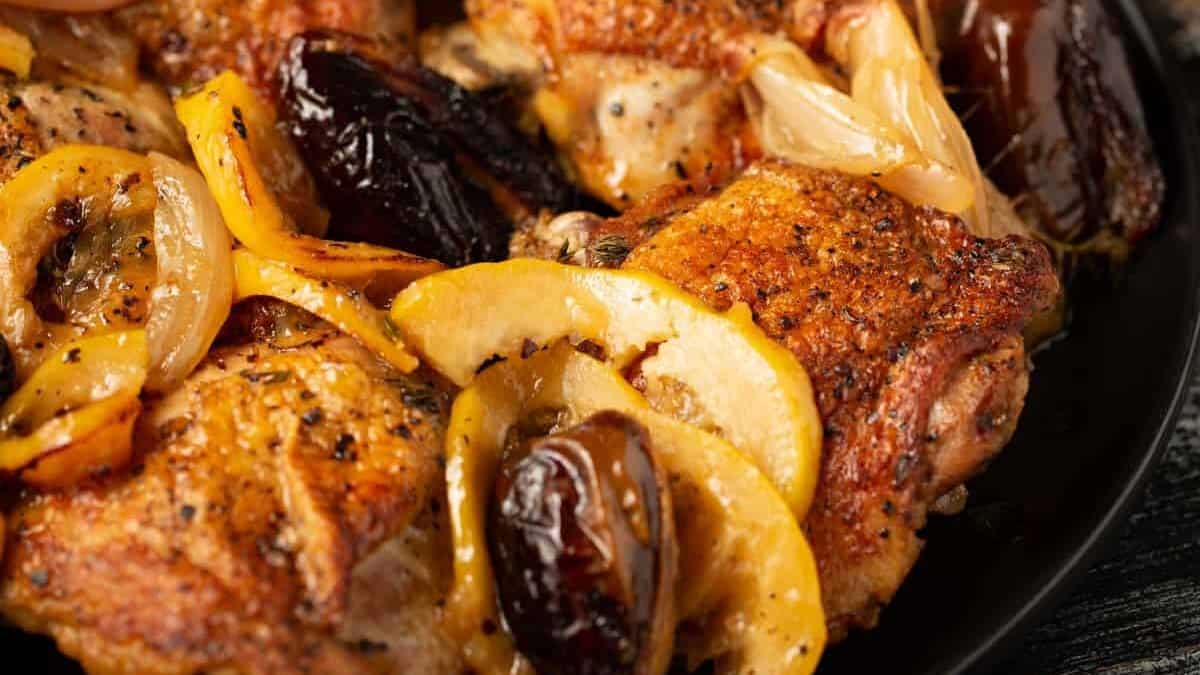 Baked lemon chicken with dates on a black platter.